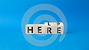 Help is here symbol. Turned wooden cubes with words Here to Help. Beautiful blue background. Business and Help is here concept.