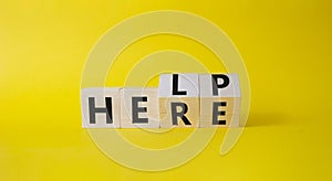 Help is here symbol. Turned wooden cubes with words Here to Help. Beautiful yellow background. Business and Help is here concept.