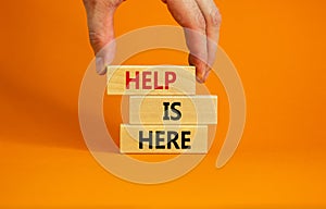 Help is here symbol. Wooden blocks with words `Help is here` on beautiful orange background. Businessman hand. Business, support