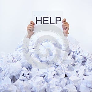 Help me. a businessman holding a help sign while buried under a pile of crumpled up paperwork.