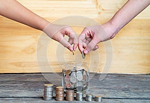 Help save money for the future. The two hands drop the coin into the savings glass, Close up hand putting coins in the stack on a