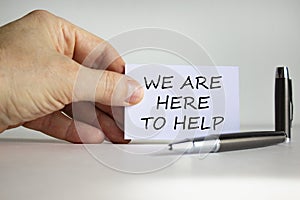 Help and support symbol. White paper with words `we are here to help` in businessman hand, metalic pen. Beautiful white backgrou