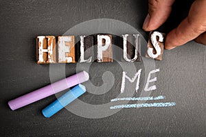 Help Us and Help Me concept. Wooden letters and colored pieces of chalk on a dark blackboard