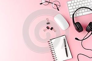 Helpdesk desktop with headset, computer and accessories. Pink business background with copyspace