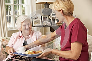 Helper Serving Senior Woman With Meal In Care Home