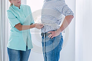 Helpful dietitian measures the patient`s waist circumference during the examination photo