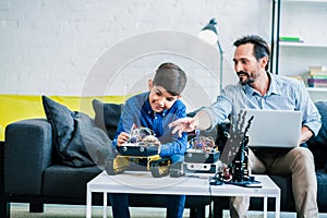 Helpful positive man helping his son with robotic engineering