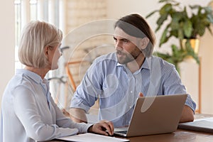 Helpful team leader helping mature employee with corporate software