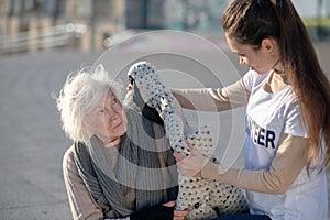 Helpful volunteer bringing warm coat for homeless woman