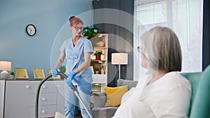 helping elderly, a young female nurse for elderly in a medical suit helps an old woman with cleaning house