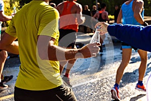 A helping hand delivers a bottle of water to a runner in a running race for him to drink