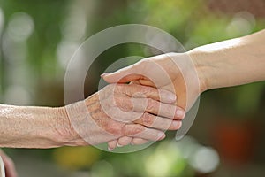 Young caregiver holding seniors hands. Helping hands, care for the elderly concept