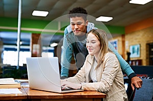 Helping one another prep for finals. a young man looking on while a female student works on a laptop.