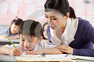 Helping Student Working At Desk In Chinese School