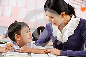 Helping Student Working At Desk In Chinese School