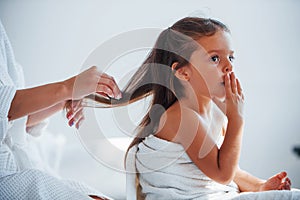 Helping to made hairstyle. Young mother with her daugher have beauty day indoors in white room