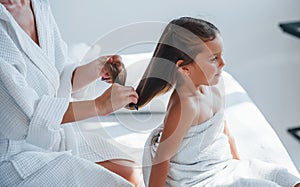 Helping to made hairstyle. Young mother with her daugher have beauty day indoors in white room