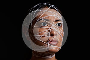 Helpless and afraid. a young woman wrapped in string against a dark background.