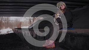 Helpless little houseless girl with toy sits in winter under bridge.