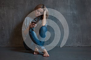 Helpline, psychological assistance. Suffering young woman sitting in a corner with a phone in her hand.