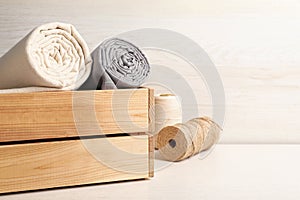 Hemp cloths in crate and threads on white wooden table, space for text