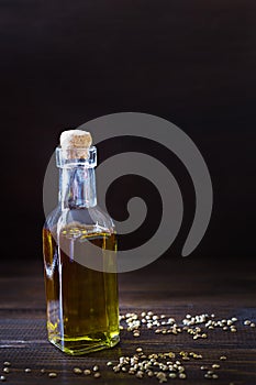 Hemp oil in a glass bottle and seeds on a dark wooden background. Vertical photo.