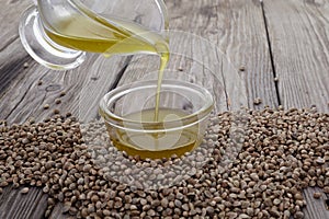 Hemp oil in a glass bowl and seeds on wooden background