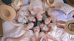 Hen party, girls in pajamas with straw hats on faces lie on bed and then take off them and smile into camera indoors