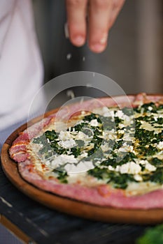 The hend of cook is decorating pizza with cheese and herbs