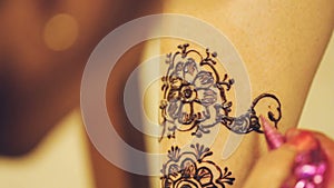 Henna artist painting tattoo on indian bride`s leg