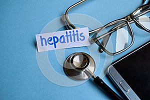 Hepatitis inscription with the view of stethoscope, eyeglasses and smartphone on the blue background