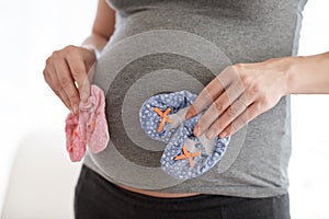 Her babys first pair. a pregnant woman holding baby shoes while standing in her home.