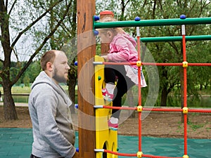 Her father is standing next to a horizontal bar on the playground