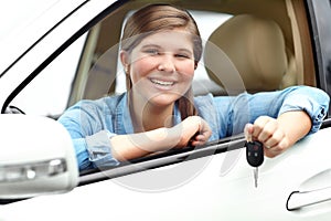 Her first car. A pretty young teenager smiling while sitting in her first car and holding the keys.