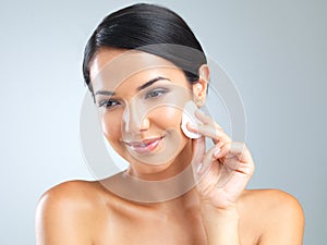 Her perfect complexion takes work. Cropped studio shot of a beautiful young woman holding a makeup pad to her face.