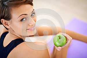 Her secret weapon to a healthy life. a sporty young woman sitting on a gym floor eating an apple.