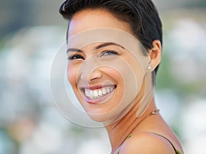 Her smile compliments her perfect complexion. Portrait of an attractive young woman standing outside.