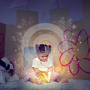 Her very first fairytale. an adorable little girl sitting on the floor and reading a glowing book.