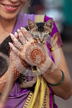 On her wedding day, the bride holds a kitten with mehndi-covered hands