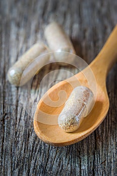 Herb capsules spilling in wooden spoon.
