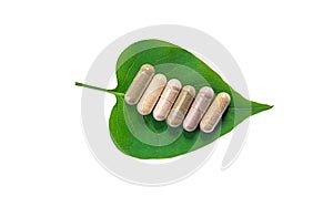 Herb supplement capsules on green leaf isolate on white background. Selective focus.