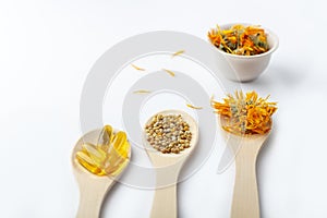 Herbal capsule, natural vitamins, dry calendula flowers at wooden spoon on white background. Concept of healthcare and alternative