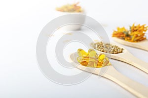 Herbal capsule, natural vitamins, dry calendula flowers at wooden spoon on white background. Concept of healthcare and alternative