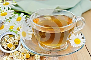Herbal chamomile tea in cup with strainer on board