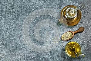 Herbal infusion fennel tea in glass cup and glass tea pot with dried fennel seeds in wooden shovel on grey rustic table