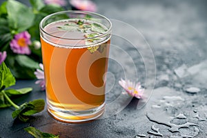 Herbal kombucha tea with floral garnish. Kombucha in a glass amid blossoms. Flower accented kombucha on dark wet surface, copy