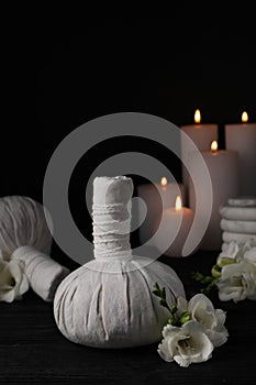 Herbal massage bags, candles, spa stones and freesia flowers on black wooden table