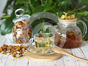 Herbal medicinal tea made from dried flowers of calendula and marigolds on a wooden table and with green leaves in the background.
