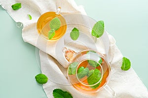 Herbal mint tea in cup and teapot on green background with mint leaves. Flat lay, top view