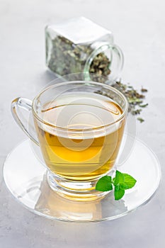 Herbal mint tea in a glass cup with dry peppermint tea on background